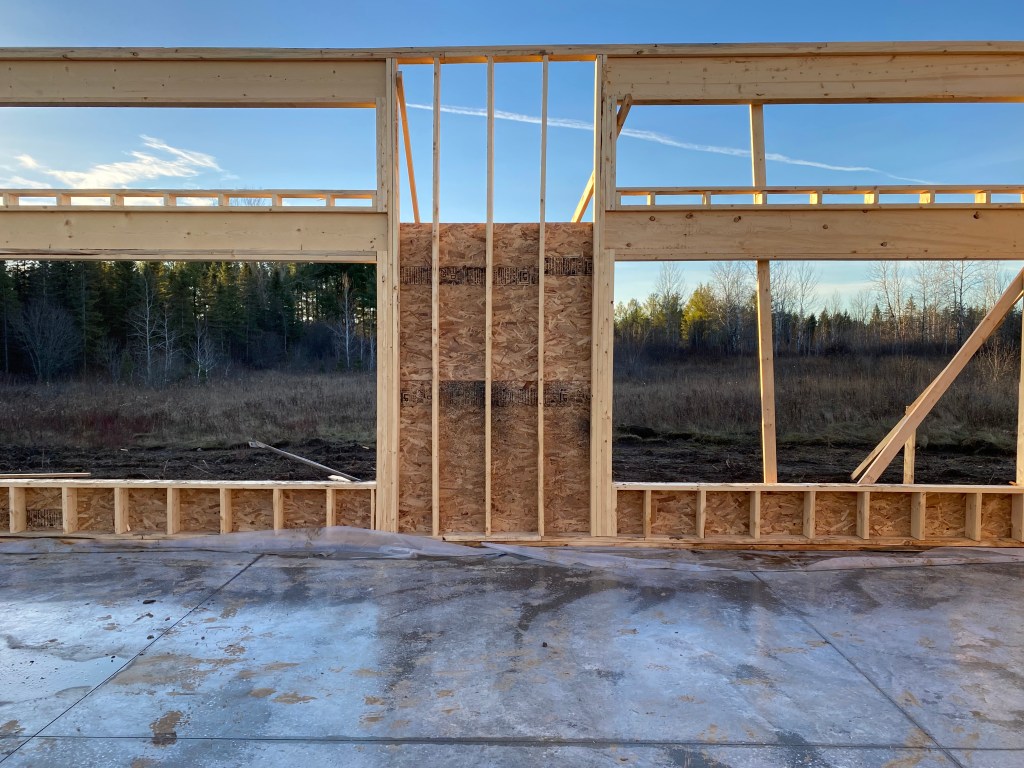 Photo of framed walls of house under construction with forest visible through window openings